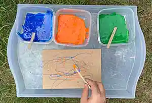 Wooden craft sticks drizzling colored glue on paper